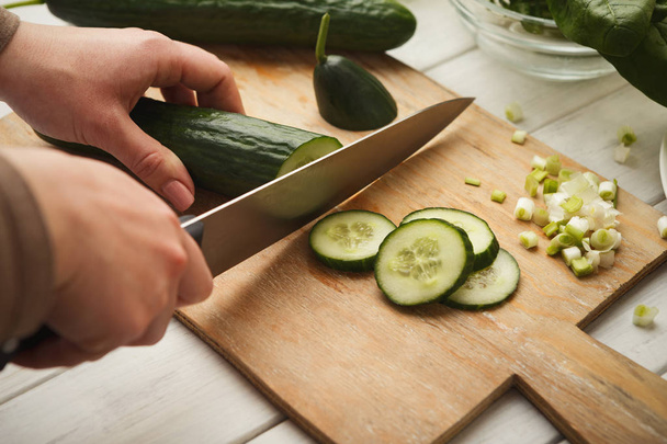 Vrouw snijden komkommer voor frisse salade bovenaanzicht - Foto, afbeelding