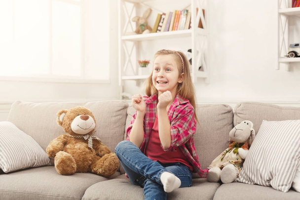 Beautiful casual little girl watching tv while sitting on sofa at home - Foto, Imagen
