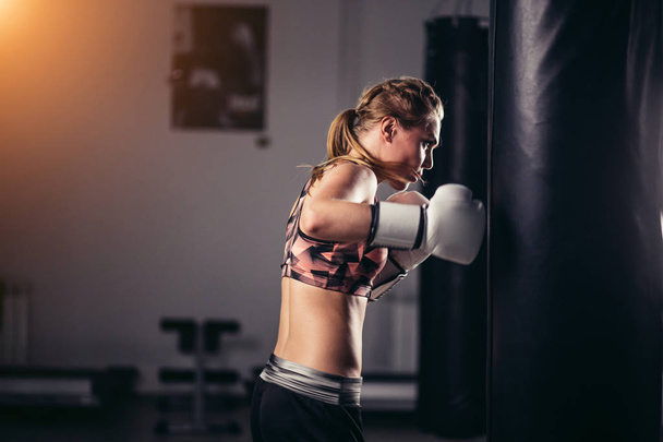 fighter girl wearing sportswear punching bag - Foto, afbeelding