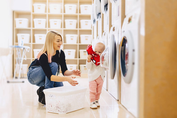 Mamá y el bebé en la lavandería toman cosas y juegan
 - Foto, Imagen