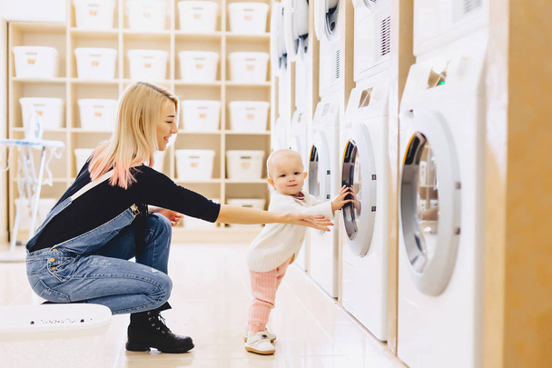 Mamá y el bebé en la lavandería toman cosas y juegan
 - Foto, imagen