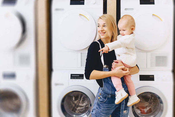 mãe com bebê no fundo de máquinas de lavar roupa
 - Foto, Imagem