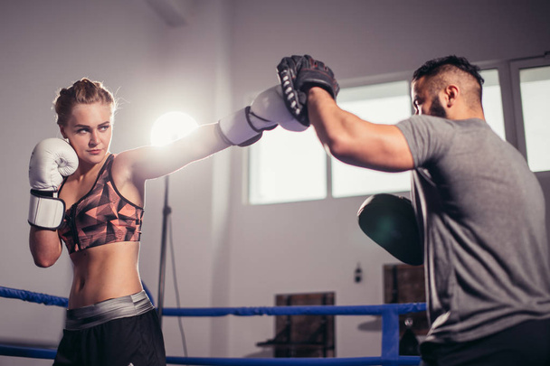 Boxing girl training on boxing mitts held by a master boxer - Foto, afbeelding