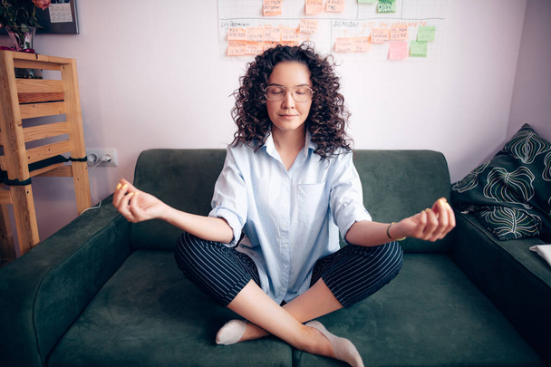 girl with wavy hair and glasses doing yoga on the sofa at home - Fotoğraf, Görsel