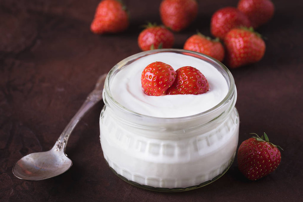 White yogurt in glass bowl with spoon and starwberries on rustic background. - Foto, immagini