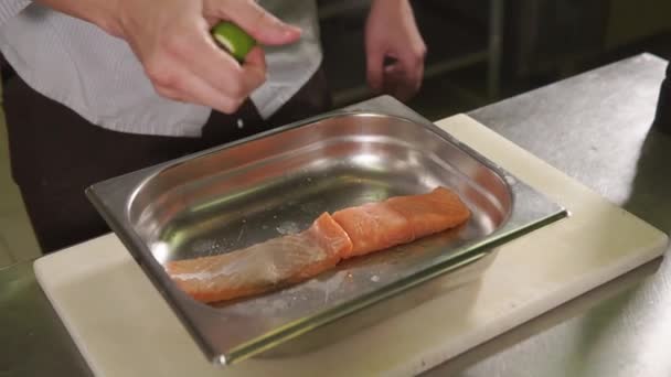 Chef está salpicando filetes de pescado con jugo de lima en una cocina profesional
 - Imágenes, Vídeo