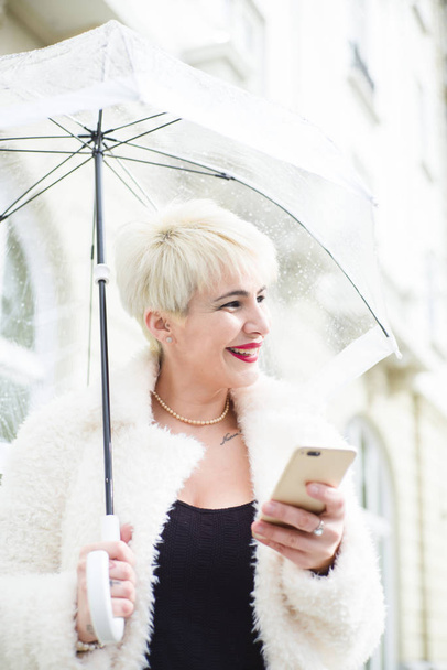 Blonde woman with umbrella texting on smartphone - Fotografie, Obrázek