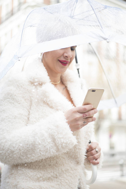 Blonde woman with umbrella texting on smartphone - Photo, Image