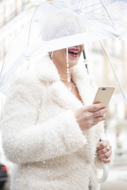 Blonde woman with umbrella texting on smartphone - Photo, Image