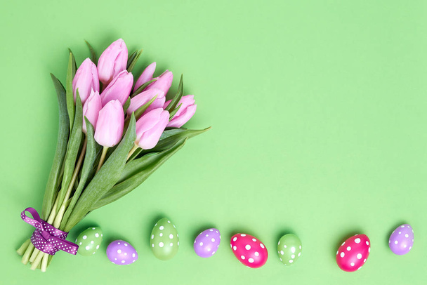 Easter background. Decorative Easter eggs and pink tulips bouquet on green background. Copy space, top view - Foto, Bild