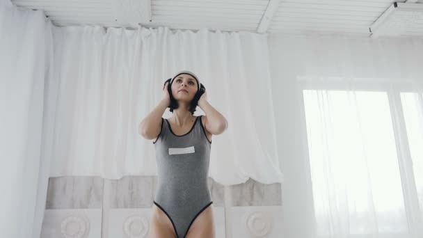 Charming woman or teenage girl in headphones a listening to music in headphones from smartphone and dancing on bed at home in a white bedroom - Footage, Video