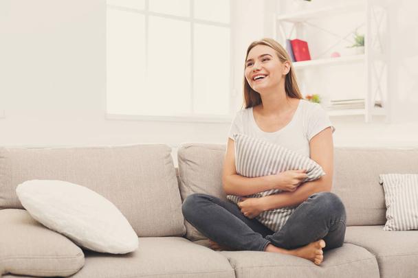 Nuori hymyilevä nainen istuu beige sohvalla
 - Valokuva, kuva