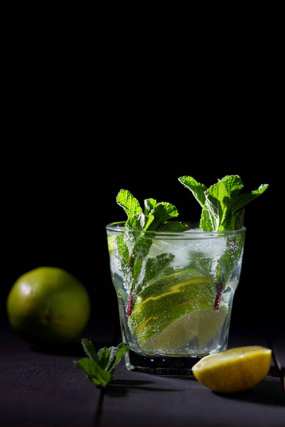 Minimalist cocktail, mojito on a dark background, summer cocktail with lime and mint, refreshing drink with lemon, fresh mint for cocktail, celebratory drink with ice, vegan, copy space, blank for designer, art - Foto, afbeelding