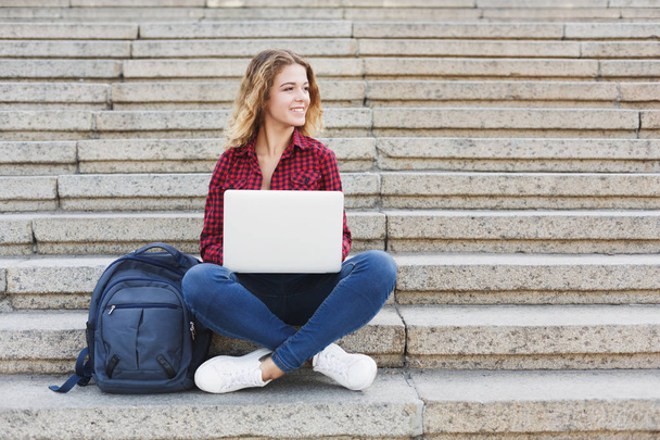 Студентка сидит на лестнице и работает с ноутбуком на открытом воздухе
 - Фото, изображение