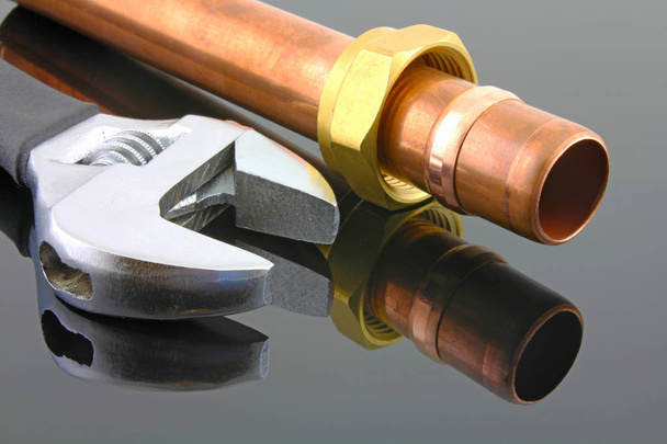 Tuyauterie en plombier Vue en plan d'une clé réglable et d'une tuyauterie en cuivre de 15 mm avec raccord de compression sur fond réfléchissant noir
 - Photo, image
