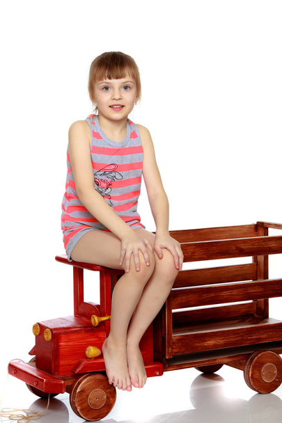 The girl is sitting on a large toy wooden car. - Φωτογραφία, εικόνα