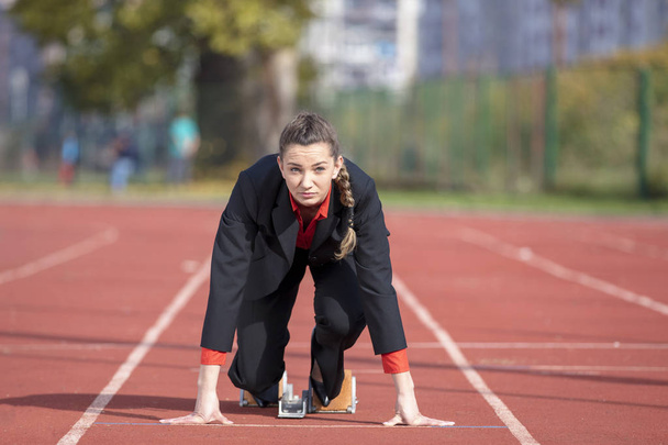 Mulher de negócios em posição de início pronto para correr e sprint no atletismo pista de corrida
 - Foto, Imagem
