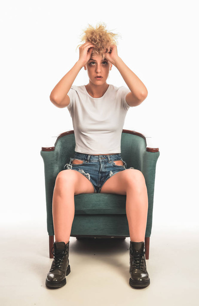 femme blonde élégante à la mode assise sur la chaise et posant devant la caméra en studio. concept de beauté de mode. isolé sur fond blanc
 - Photo, image