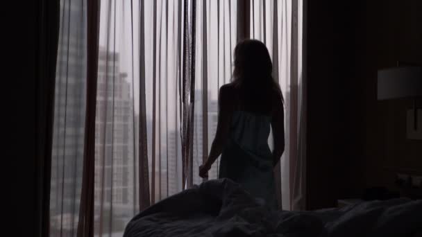 Kobieta budzi się ze snu, jadąc do okna z widokiem na wieżowce, otwiera zasłony. zwolnionym tempie. 4k - Materiał filmowy, wideo