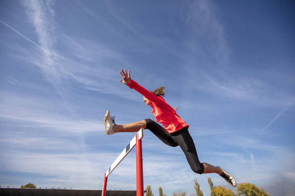 Female athlete jumping above the hurdle during the race - Foto, imagen
