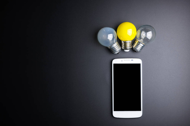 Smartphone and light bulb on black background with copy space. - Fotoğraf, Görsel