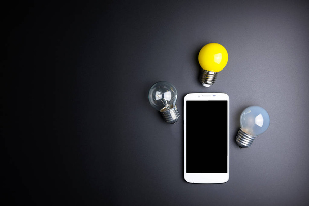 Smartphone and light bulb on black background with copy space. - Foto, imagen