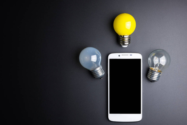 Smartphone and light bulb on black background with copy space. - Photo, image