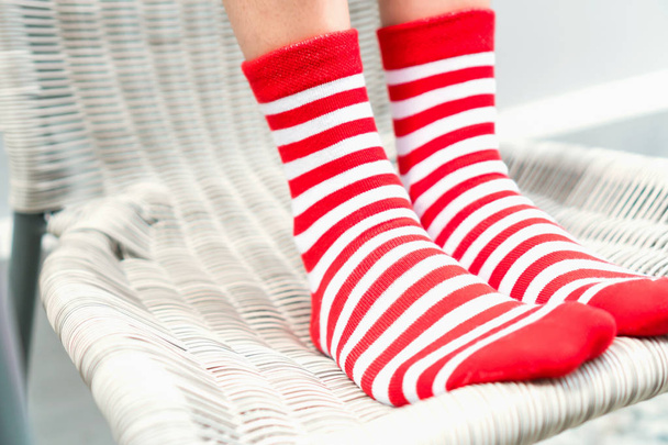 Πόδια σε κάλτσες κόκκινο χρώματα εναλλακτική, λευκή πλευρά σταθεί σε λευκή καρέκλα. - Φωτογραφία, εικόνα