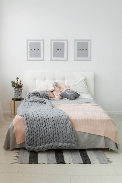 Interior de dormitorio de primavera con flores y marcos cerca de la cama gris. Decoración minimalista con luz natural
 - Foto, Imagen