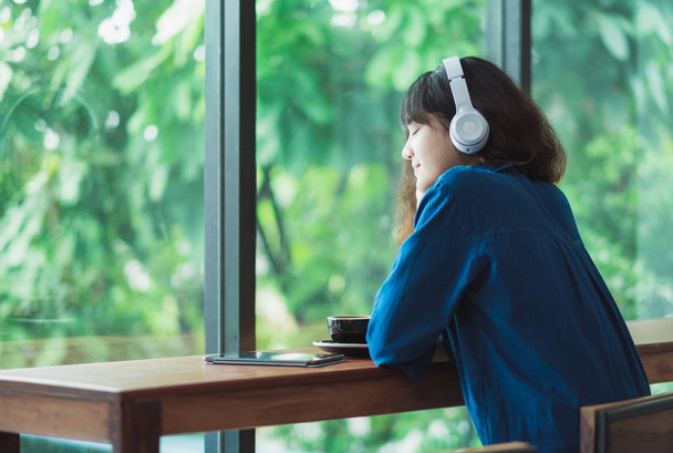 Happy asian casual woman listening music with headphones near wi - Photo, image