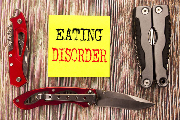 Hand writing text caption inspiration showing Eating Disorder. Business concept for Medical Problem Written on sticky note wooden background with pocket knife - Photo, Image