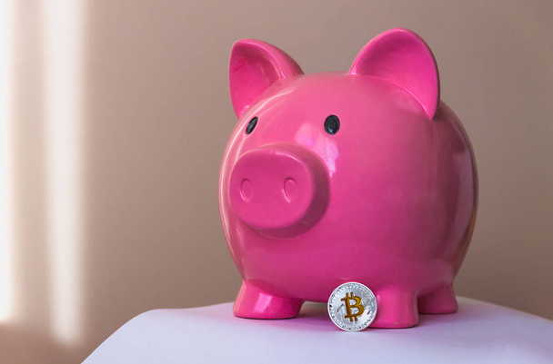 rosafarbenes Sparschwein in Form eines Schweins und einer nahegelegenen Münze Bitcoin - Foto, Bild
