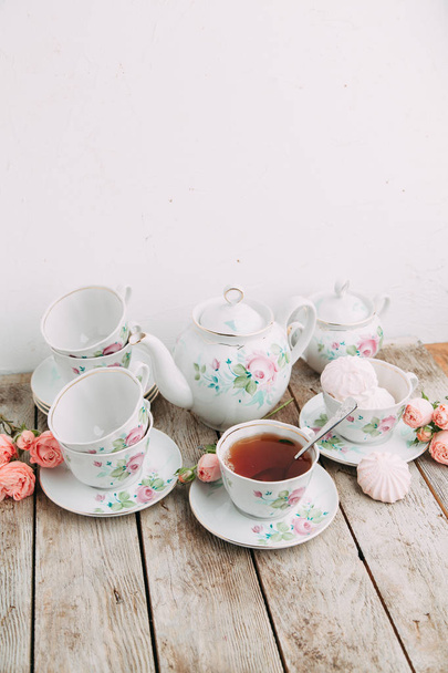 tea set in composition with flowers and marshmallows. Coffee mug on a saucer, a teapot and a sugar bowl. Filmed in the interior - Фото, изображение