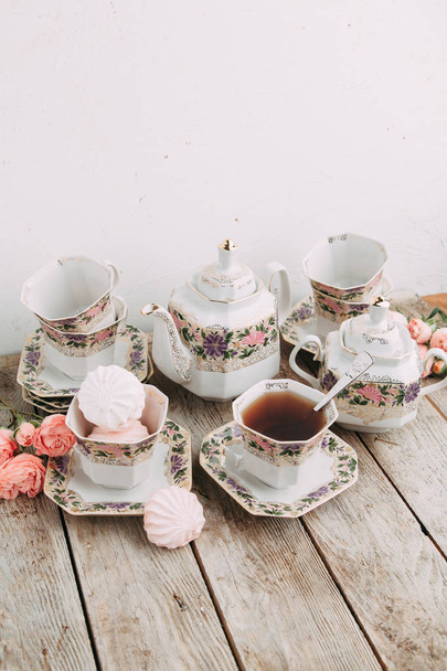 tea set in composition with flowers and marshmallows. Coffee mug on a saucer, a teapot and a sugar bowl. Filmed in the interior - Photo, image