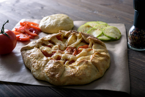 freshly baked Galeta with vegetables and cheese on a wooden table with ingredients, olive oil, red pepper, tomatoes and raw dough - Photo, image