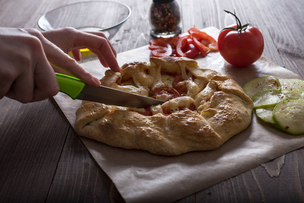 女性の手は、ズッキーニ、トマト、チーズと新鮮な野菜のパイをカットします。 - 写真・画像
