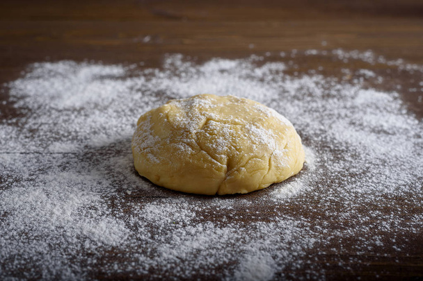 Raw dough ball sprinkled with white flour on a wooden table. - Photo, Image
