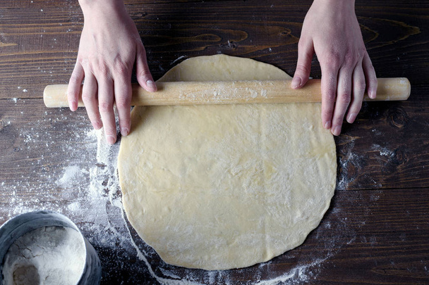 Women's hands roll out rolling pin dough on a wooden table, side light, Flatley, top view - Photo, image