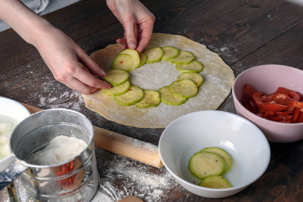 野菜のピザを作るプロセス [トップ ビューで、女性の手に広がる生地のズッキーニ - 写真・画像