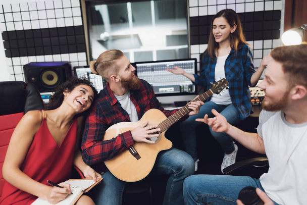 Two women and two men sing a song in a guitar in a modern recording studio. They sit behind the remote control of sound and sing a song. They are having fun. - Photo, Image