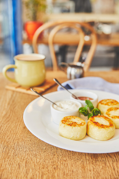 Panqueques de queso servidos con miel y crema agria en la mesa con café
 - Foto, imagen