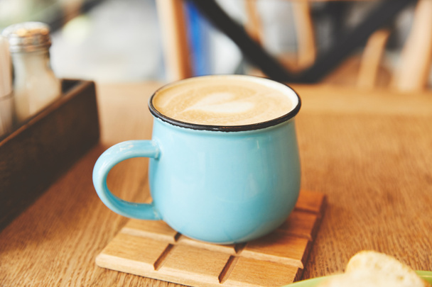 Hot cappuccino in blue mug on table - Fotografie, Obrázek
