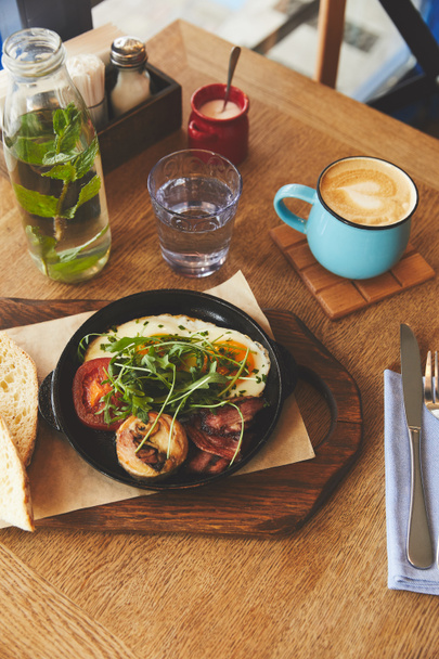 Śniadanie z jajkiem sadzonym, serwowane w patelni z kawy na stole - Zdjęcie, obraz
