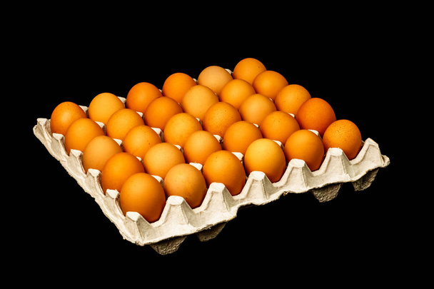 Ryhmä tuoreita munia mustalla pohjalla eristetyllä paperilaatikolla
 - Valokuva, kuva