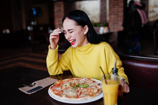 Funny brunette girl in yellow sweater eating pizza at restaurant - Zdjęcie, obraz