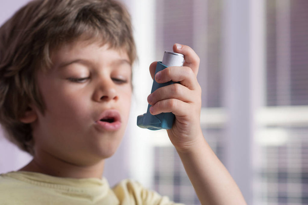 Αγόρι συσκευή εισπνοής άσθμα χρήση για τη θεραπεία της φλεγμονώδους νόσου, συριγμό, βήχα, σφίξιμο στο στήθος και δύσπνοια. Αλλεργία θεραπεία έννοια. Επιλεκτική εστίαση στη συσκευή εισπνοής. - Φωτογραφία, εικόνα