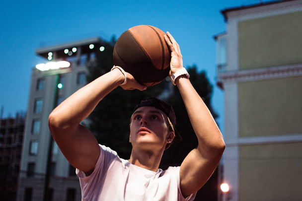 Ein Schuss. Nahaufnahme eines jungen Mannes in Sportbekleidung, der auf einem Basketballfeld im Freien Basketball spielt - Foto, Bild