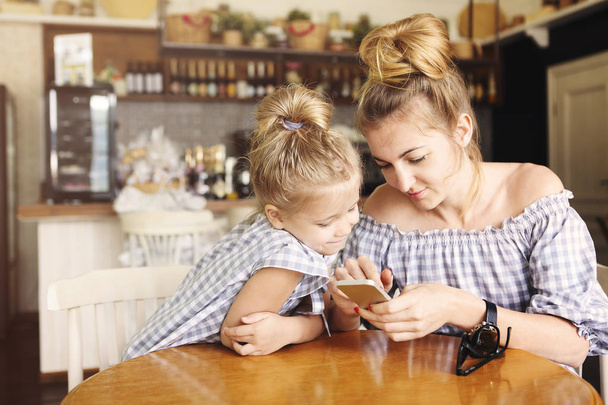  Mutlu anne ve akşam yemeği ve smartphone kullanarak küçük kız - Fotoğraf, Görsel