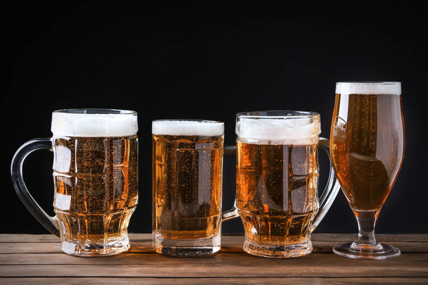 Glassware with beer on wooden table against black background - Φωτογραφία, εικόνα