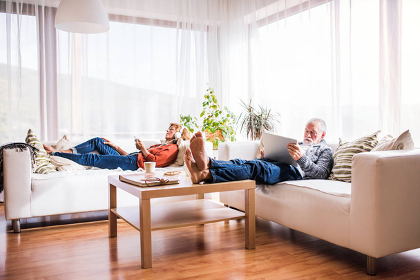 Senior couple with tablet and smartphone relaxing at home. - Фото, изображение